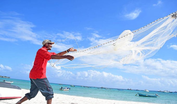 Man Casting Fishing Net into Sea